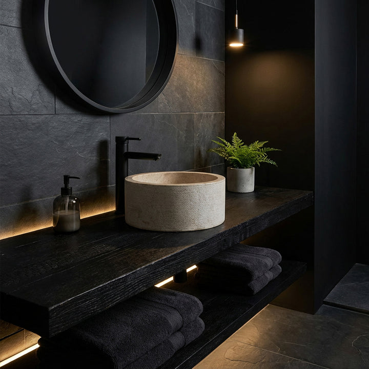 Rundes Aufsatzwaschbecken in edler Marmoroptik auf dunkler Holzkonsole, inszeniert im minimalistischen Dark-Mood-Bad.