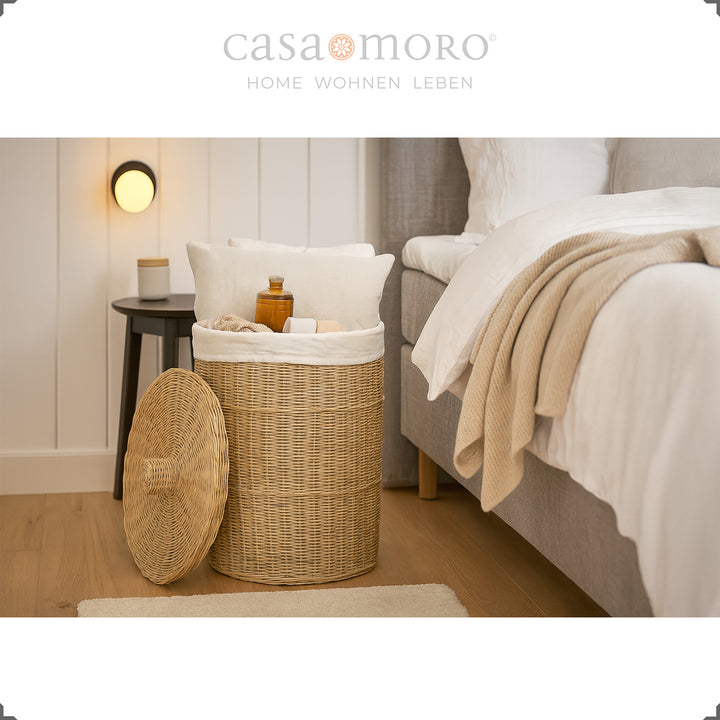Runder Rattan Wäschekorb mit Deckel im Schlafzimmer, gefüllt mit Kissen, Decken und Pflegeartikeln